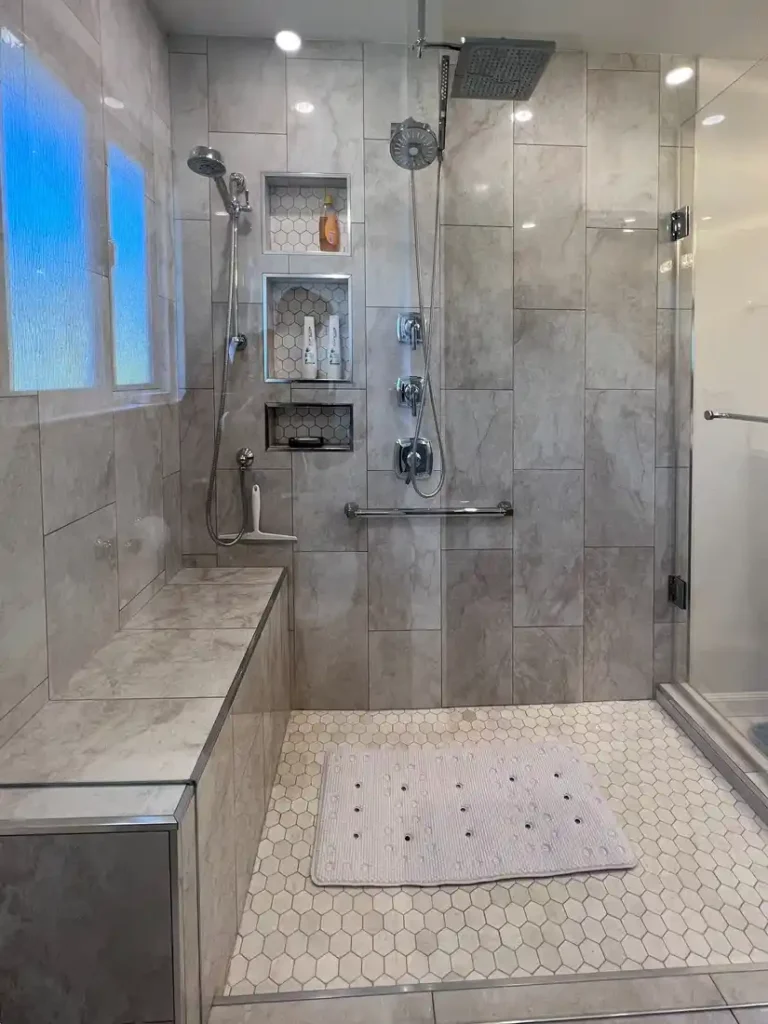 Built-in bench and three hexagon tile niches in the marble-look walk-in shower of an Aliso Viejo bathroom.