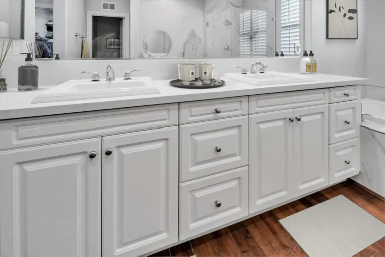 White raised-panel double vanity with quartz countertop and full-width mirror in a Carlsbad primary bathroom.