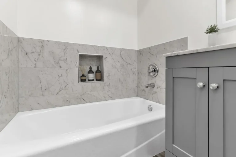 White alcove bathtub with marble tile surround and recessed niche beside a gray vanity in an Irvine bathroom remodel