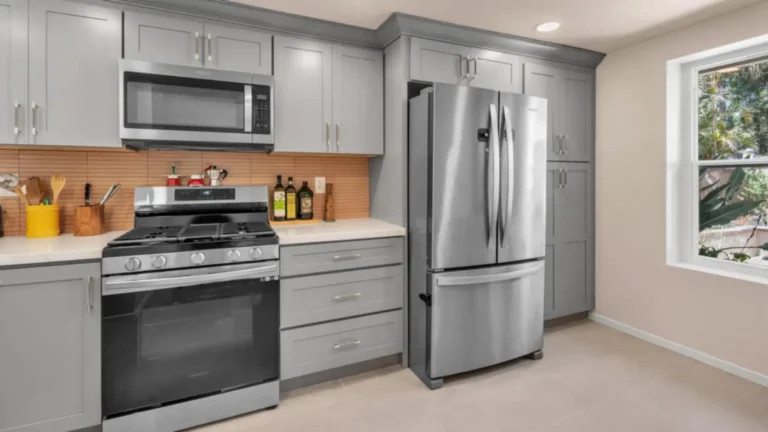 French door refrigerator set into a tall gray pantry wall beside a stainless gas range in a Carlsbad kitchen remodel