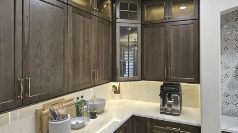 Corner of dark wood cabinets with glass doors and under-cabinet lighting on marble counters in a Costa Mesa kitchen