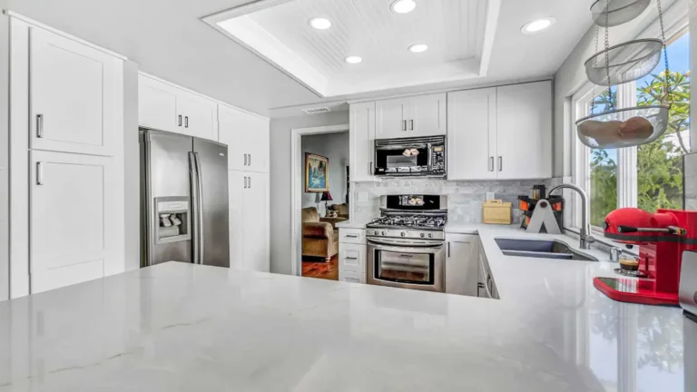White quartz peninsula countertop facing a stainless refrigerator, pantry cabinets, and gas range in an Irvine kitchen.