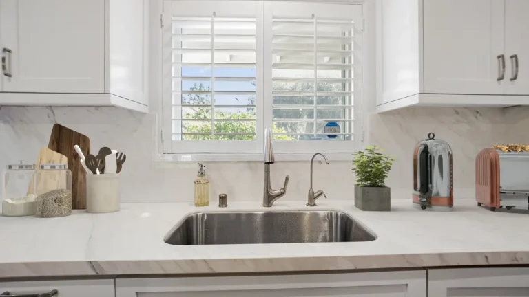 Undermount stainless steel sink below plantation shutters with a white veined slab backsplash in a Laguna Niguel kitchen