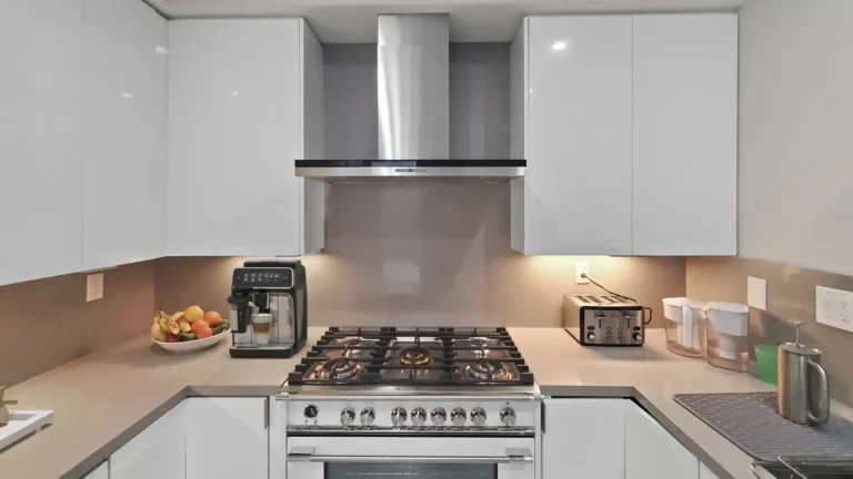 Stainless chimney hood over a white gas range and quartz slab backsplash in a U-shaped Mission Viejo kitchen