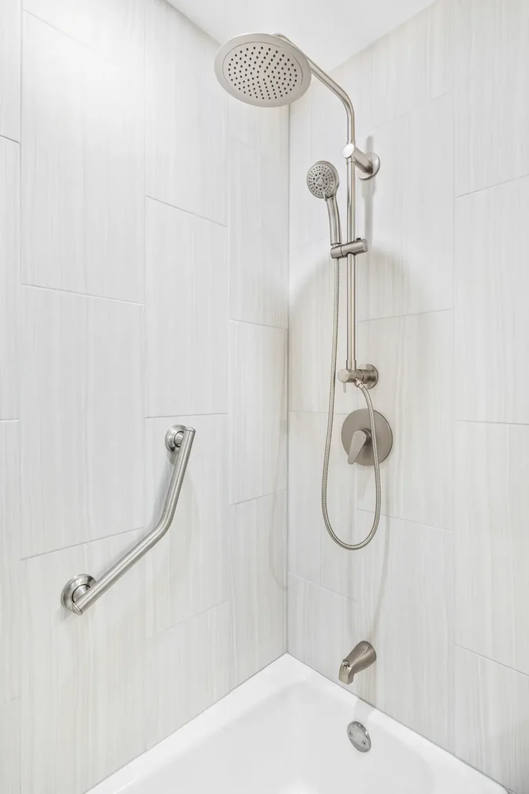 Close-up of a brushed nickel rain shower system with handheld wand on a slide bar in a Mission Viejo guest bath