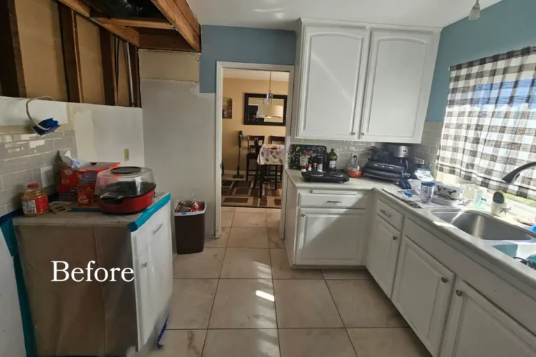 Before photo of a dated Mission Viejo kitchen with white cabinets, beige floor tile and an open wall during demolition