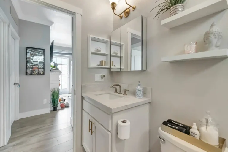 Brass wall sconce above a marble vanity with gold cabinet hardware in a Newport Beach guest bathroom remodel