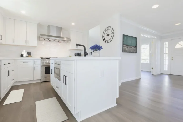 White shaker island facing a stainless range and chimney hood, open to the front entry, in a Newport Beach kitchen