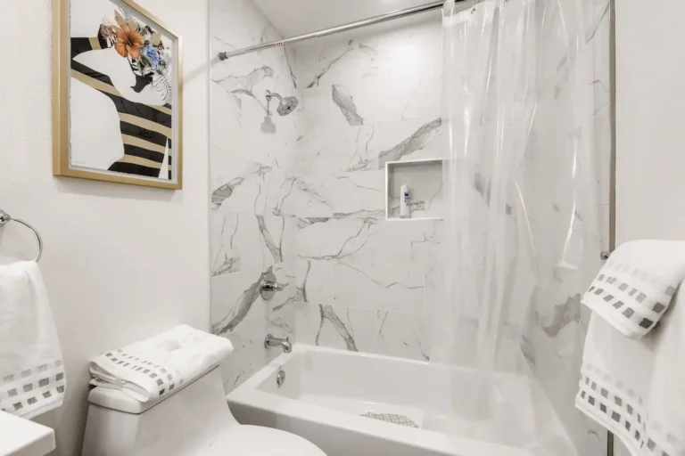 Tub and shower combo with marble look tile and a recessed niche in a remodeled San Clemente guest bathroom