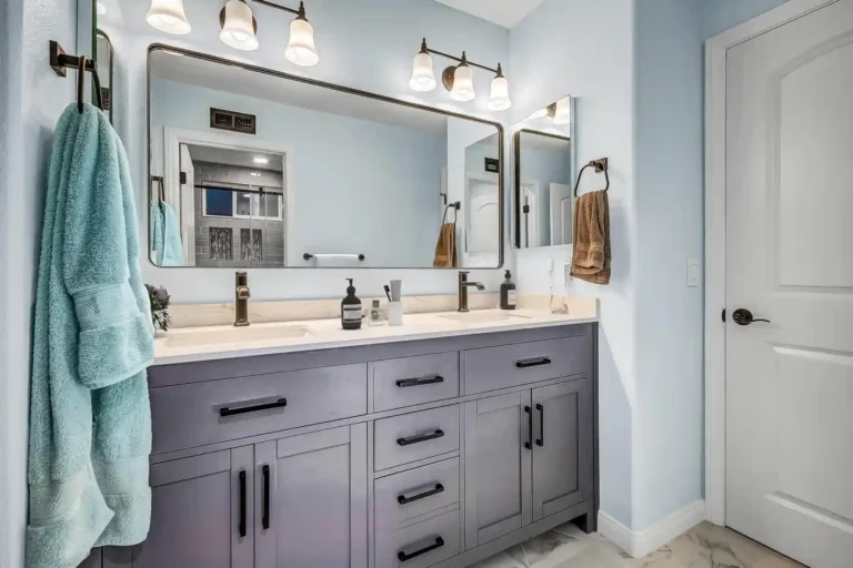 Double sink vanity with quartz countertop and a wide framed mirror in a light blue San Clemente bathroom remodel