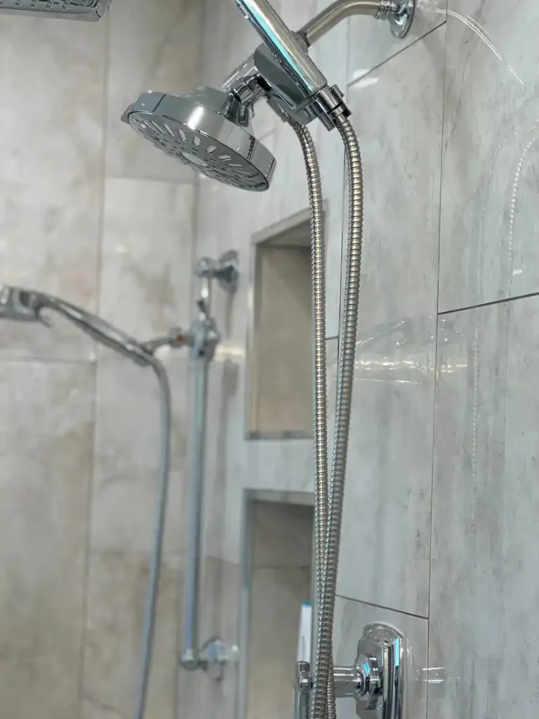 Chrome handheld shower head on a flexible hose against marble-look porcelain tile in an Aliso Viejo bathroom.