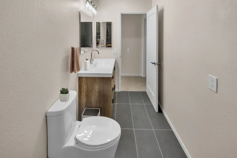 Carlsbad bathroom remodel with a wood-look vanity, mirror light bar, new toilet, and gray floor tile