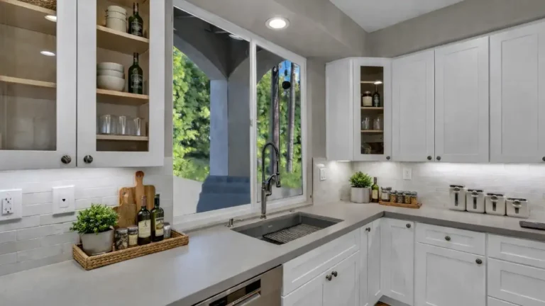 Gray undermount sink with a pull-down faucet below a window, flanked by glass-front cabinets, in a Carlsbad kitchen.