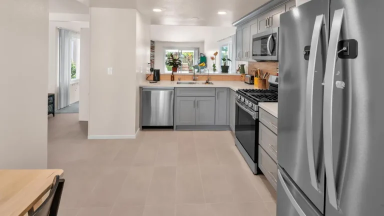 Wide view of a U-shaped Carlsbad kitchen remodel with large-format floor tile, gray cabinets, and stainless appliances