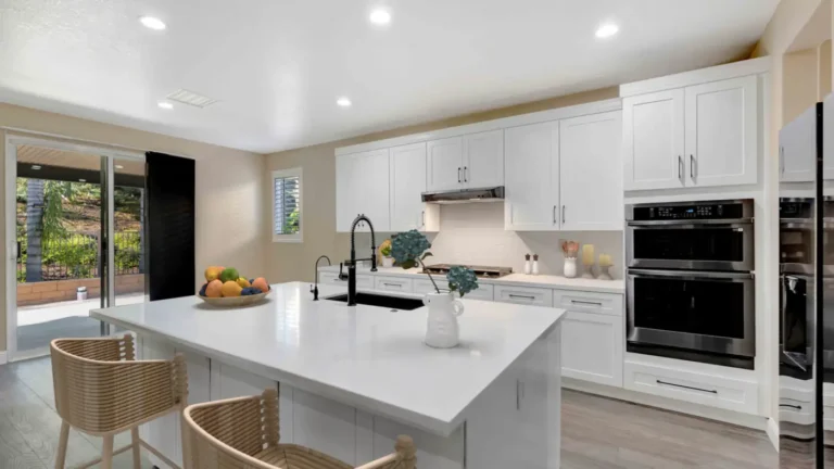 Quartz island with black spring faucet and patio slider view beside double wall ovens in a remodeled Corona kitchen