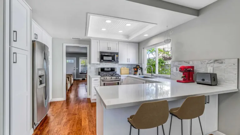 Remodeled Irvine kitchen with white shaker cabinets, a quartz peninsula, a stainless refrigerator, and hardwood floors.