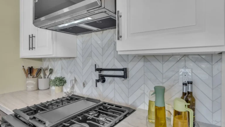 Close view of a black pot filler set in white marble chevron tile above a gas range in an Oceanside kitchen