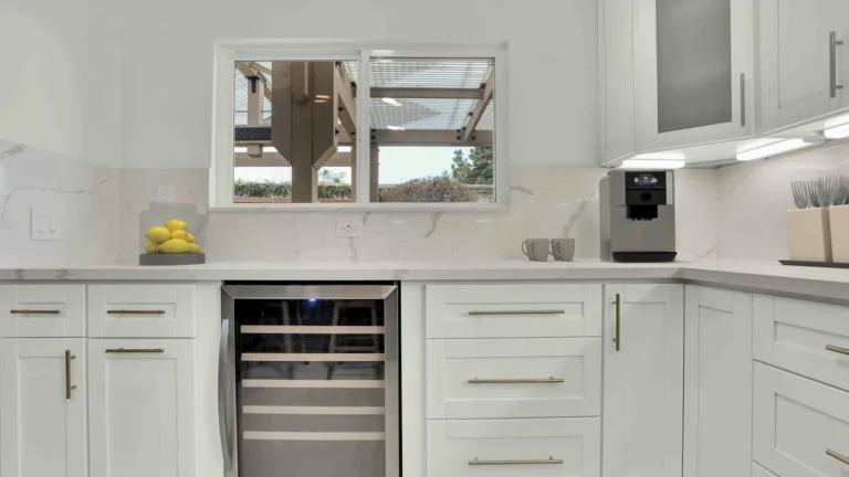 Built-in stainless wine cooler between white shaker drawer banks under a quartz countertop in an Oceanside kitchen