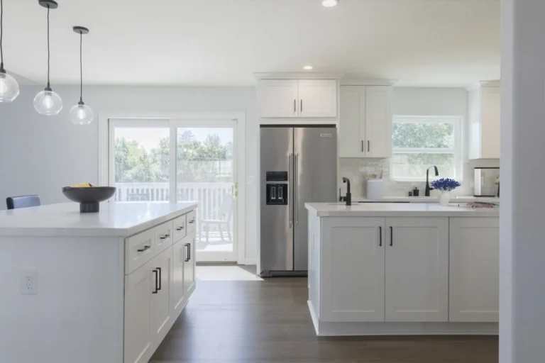 Stainless side-by-side refrigerator between two white quartz islands and a sliding patio door in a Newport Beach kitchen