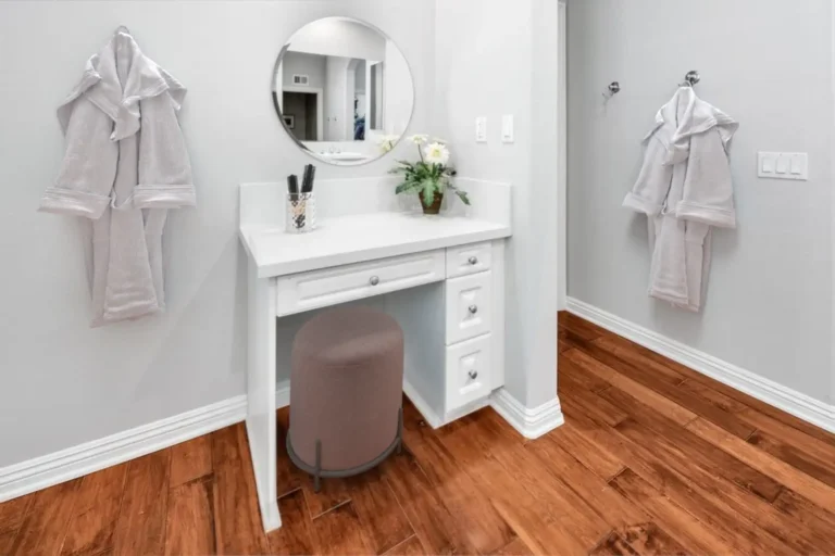 Built-in makeup vanity with a round mirror and upholstered stool in a remodeled Carlsbad primary bathroom.
