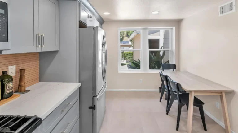 Bright dining nook with double-hung windows next to gray cabinets and a French door refrigerator in a Carlsbad kitchen