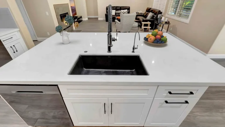 Black undermount sink with a spring faucet on a white quartz island overlooking the family room in a Corona kitchen