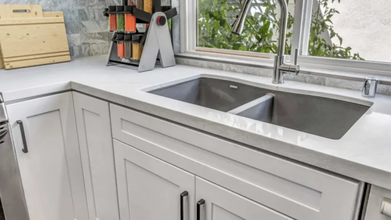 Gray double-bowl undermount sink and pull-down faucet set in white quartz beneath a window in an Irvine kitchen.