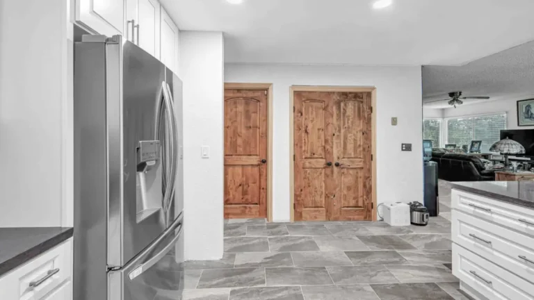 Rustic wood double doors and large gray tile floors at the edge of a remodeled Laguna Hills kitchen with white cabinets