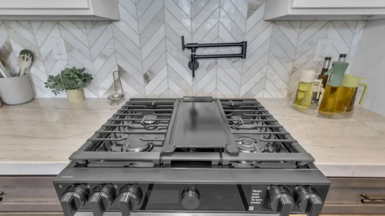 Gas range with a center griddle below a black pot filler and marble chevron tile in an Oceanside kitchen remodel