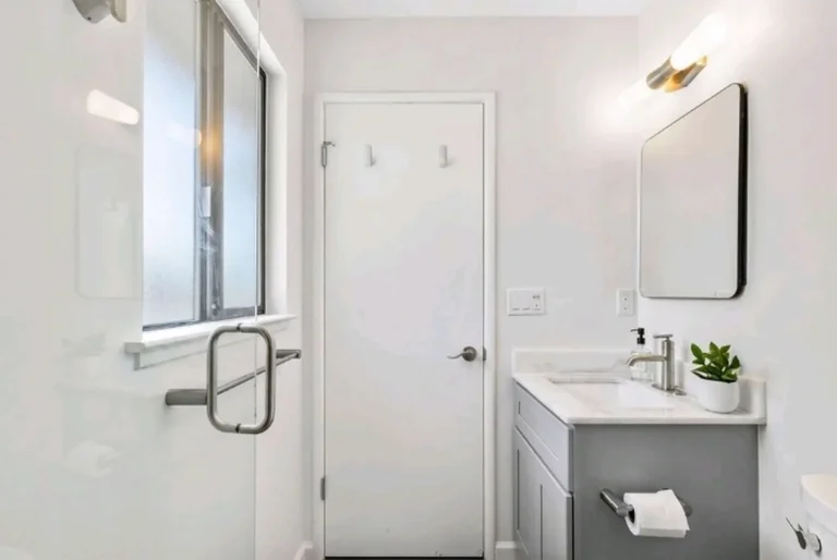 Laguna Niguel bathroom remodel with a frosted glass shower window, gray vanity, wall sconce, and glass door