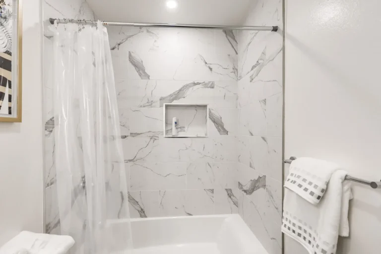Marble look tile surround with a built in shampoo niche above the tub in a San Clemente guest bathroom remodel