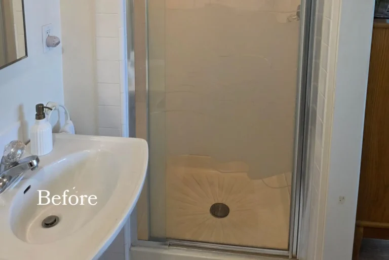 Before photo of a dated Cypress master bathroom with a framed sliding glass shower enclosure, white square tile, and a wall mounted sink