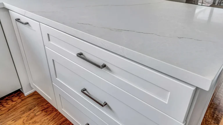 Close-up of veined white quartz countertop over white shaker drawers with brushed metal pulls in an Irvine kitchen.