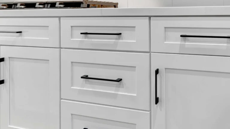 Close view of white shaker drawers and doors with matte black bar pulls below a gas cooktop in a Corona kitchen