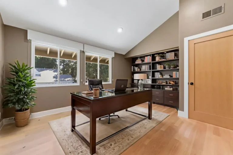 Santa Ana home office with a vaulted ceiling, built-in dark wood shelving, executive desk, and a natural wood door.