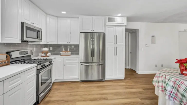 L-shaped run of white raised panel cabinets with a gas range and stainless refrigerator in a Santa Ana kitchen