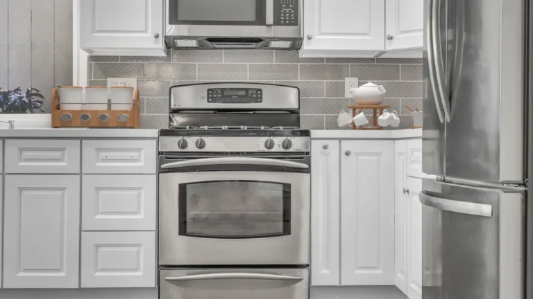 Stainless gas range and over-the-range microwave framed by white cabinets and gray tile in a Santa Ana kitchen